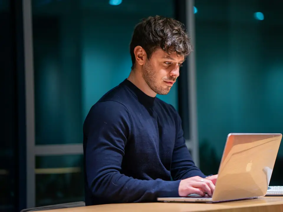 Profissional trabalhando no notebook à noite, num escritório escuro